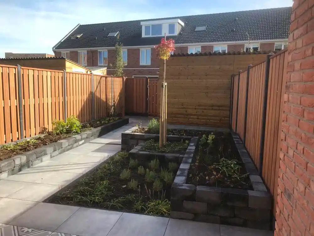 Twee verhoogde borders met lavendel en siergrassen langs een tegelpad, met een hardhouten schutting en een bakstenen muur aan weerszijden