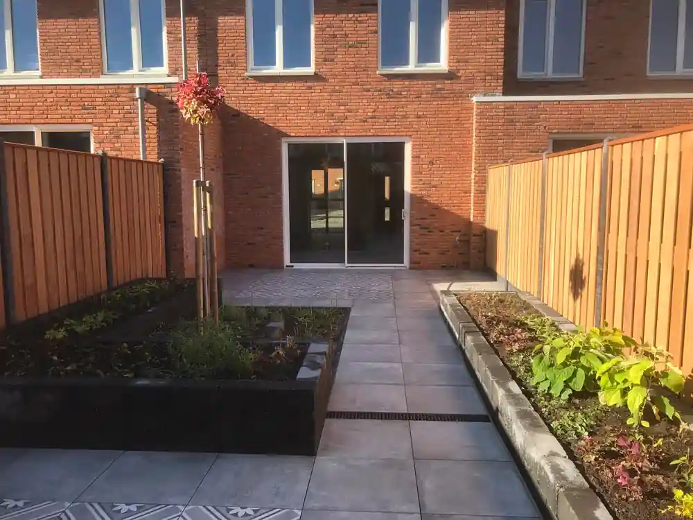 Tegelpad met lijngoot tussen twee beplante borders, met zicht op de schuifpui en een vlak patroontegels voor de woning