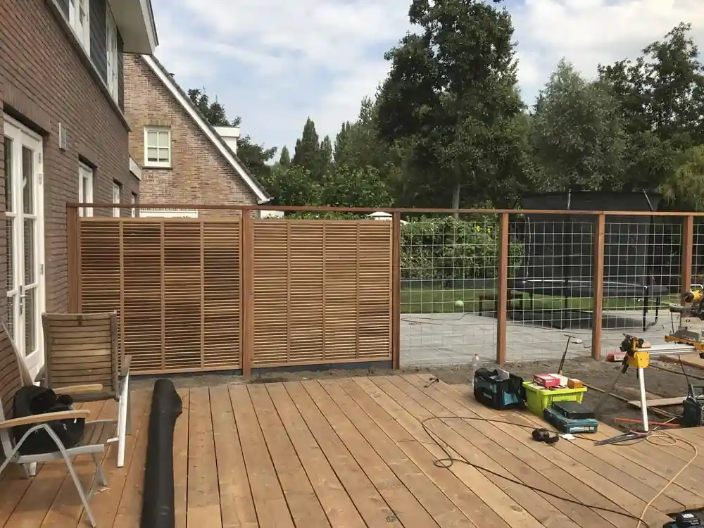 Hardhouten lattenschermen en gaaspanelen op de erfgrens naast de nieuwe vlonder, met gereedschap op de vloer tijdens de aanleg