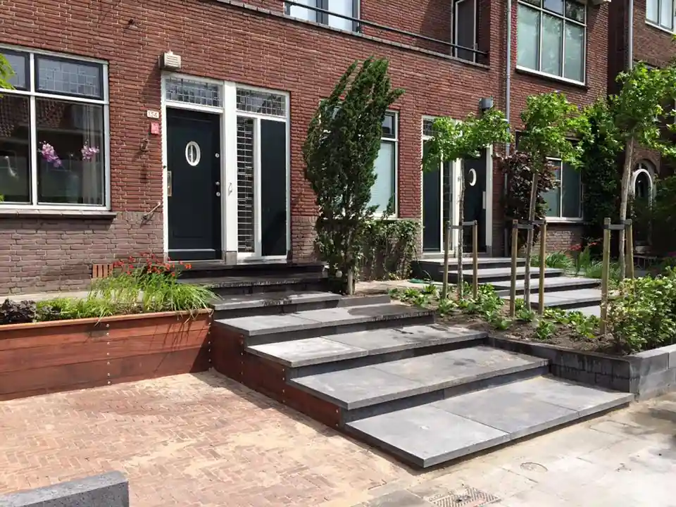 Trappartij van antracieten traptreden tussen een hardhouten plantenbak met siergrassen en een border met zuilvormige conifeer en jonge leibomen