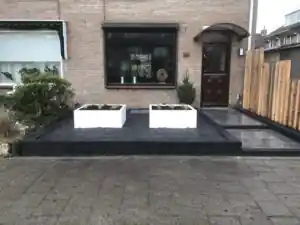 Overzicht vanaf de stoep met twee witte plantenbakken op een vlak zwart split voor de bakstenen gevel, met een Douglas scherm als erfafscheiding