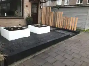 Verticaal scherm van Douglas balken op verschillende hoogtes naast twee witte plantenbakken, op een vlak zwart split met antracieten randen