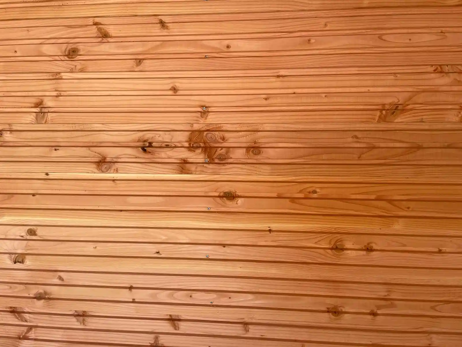 Close-up van een wand van horizontale Douglas rabatdelen met zichtbare noesten en schroeven, warm aangelicht