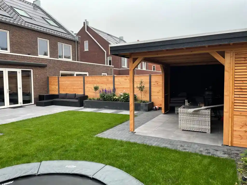 Douglas overkapping met lamellenwand en rieten loungeset, met een gazon, een verhoogde border met salie en rozen en een loungebank langs de woning