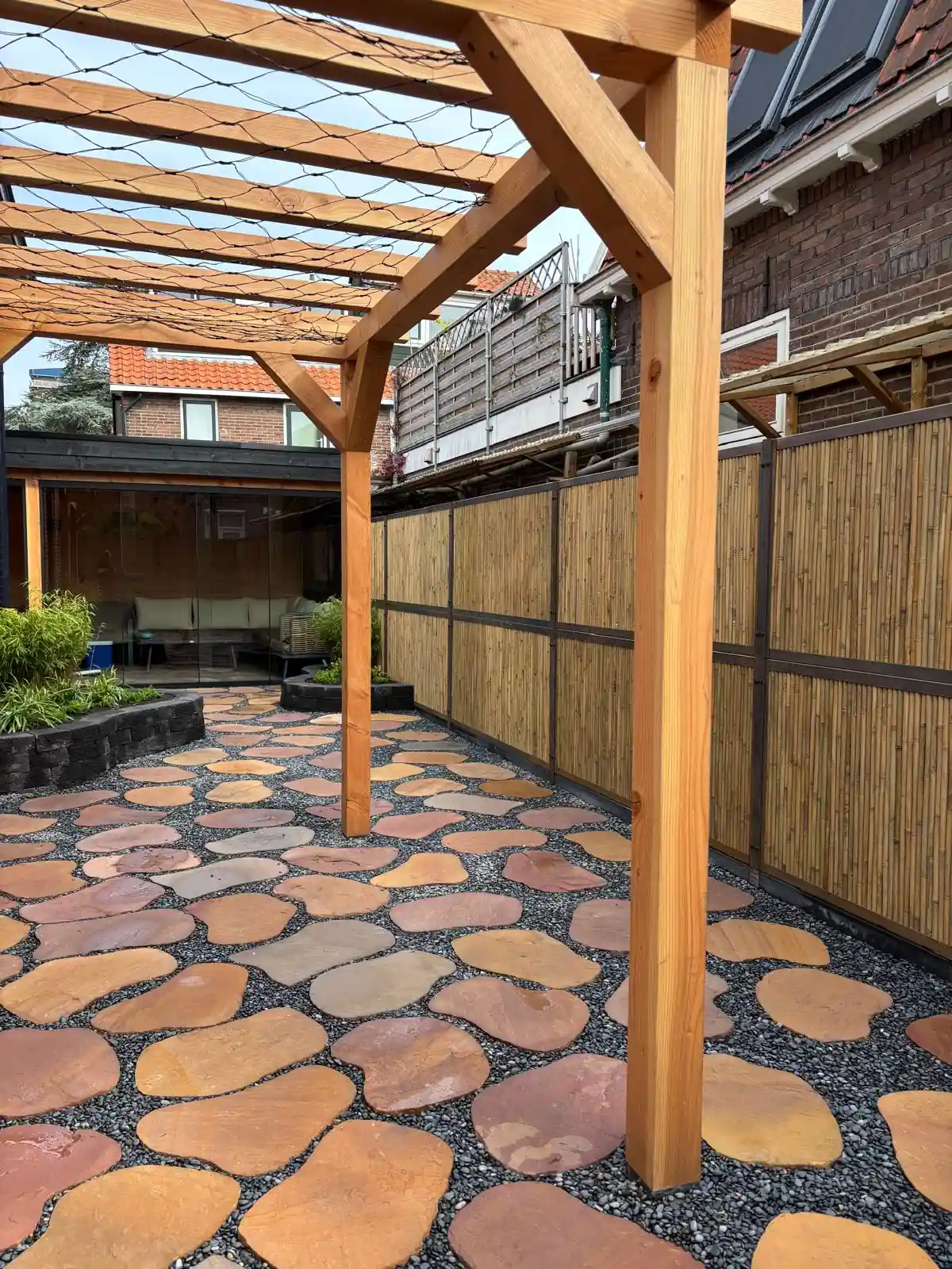 Douglas pergola met een gespannen net voor klimplanten, boven een terras van flagstones in split met zicht op de tuinkamer