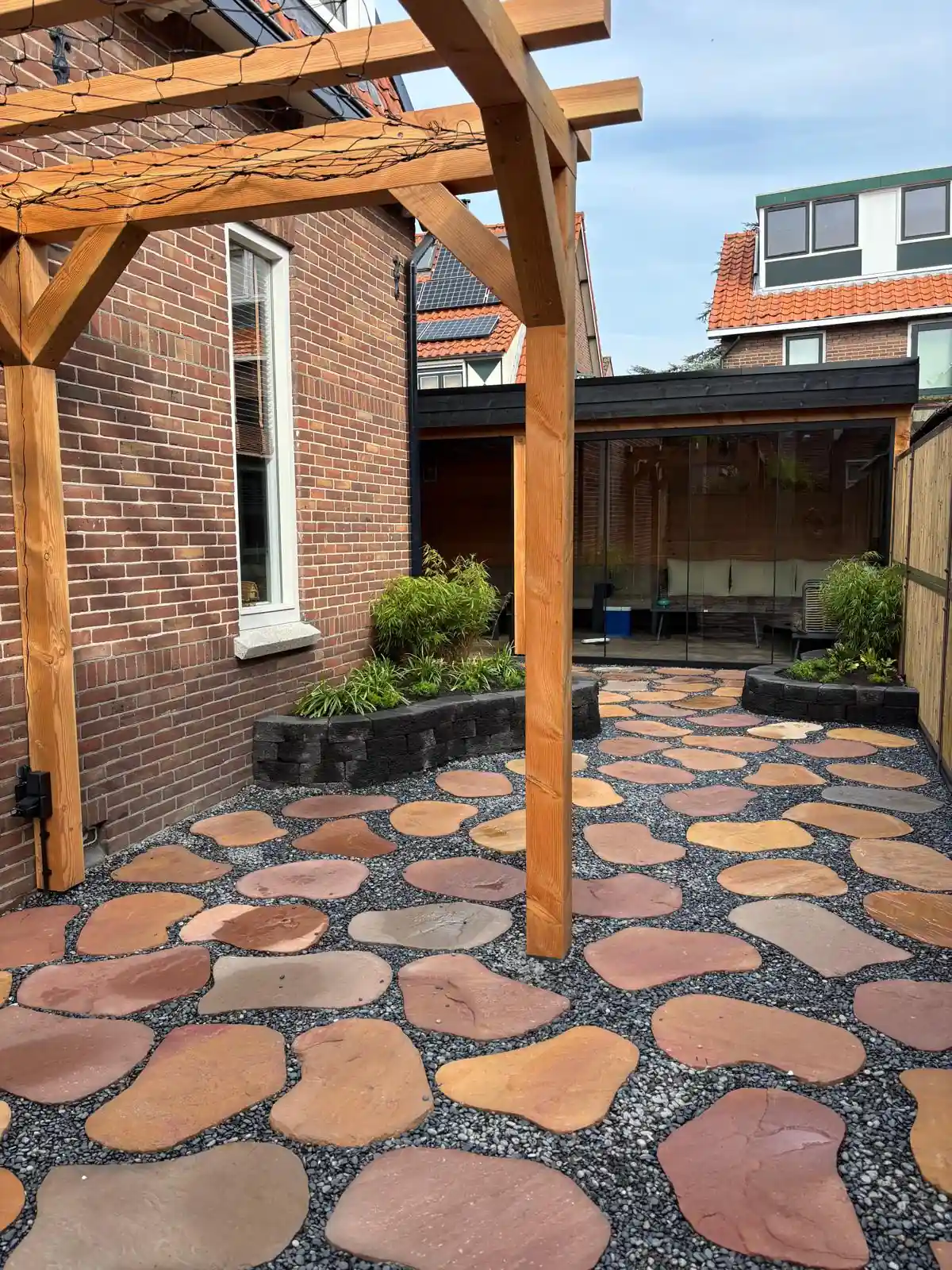 Douglas pergola langs een rode bakstenen gevel, met verhoogde borders met bamboe en een ruim terras van flagstones in grijs split