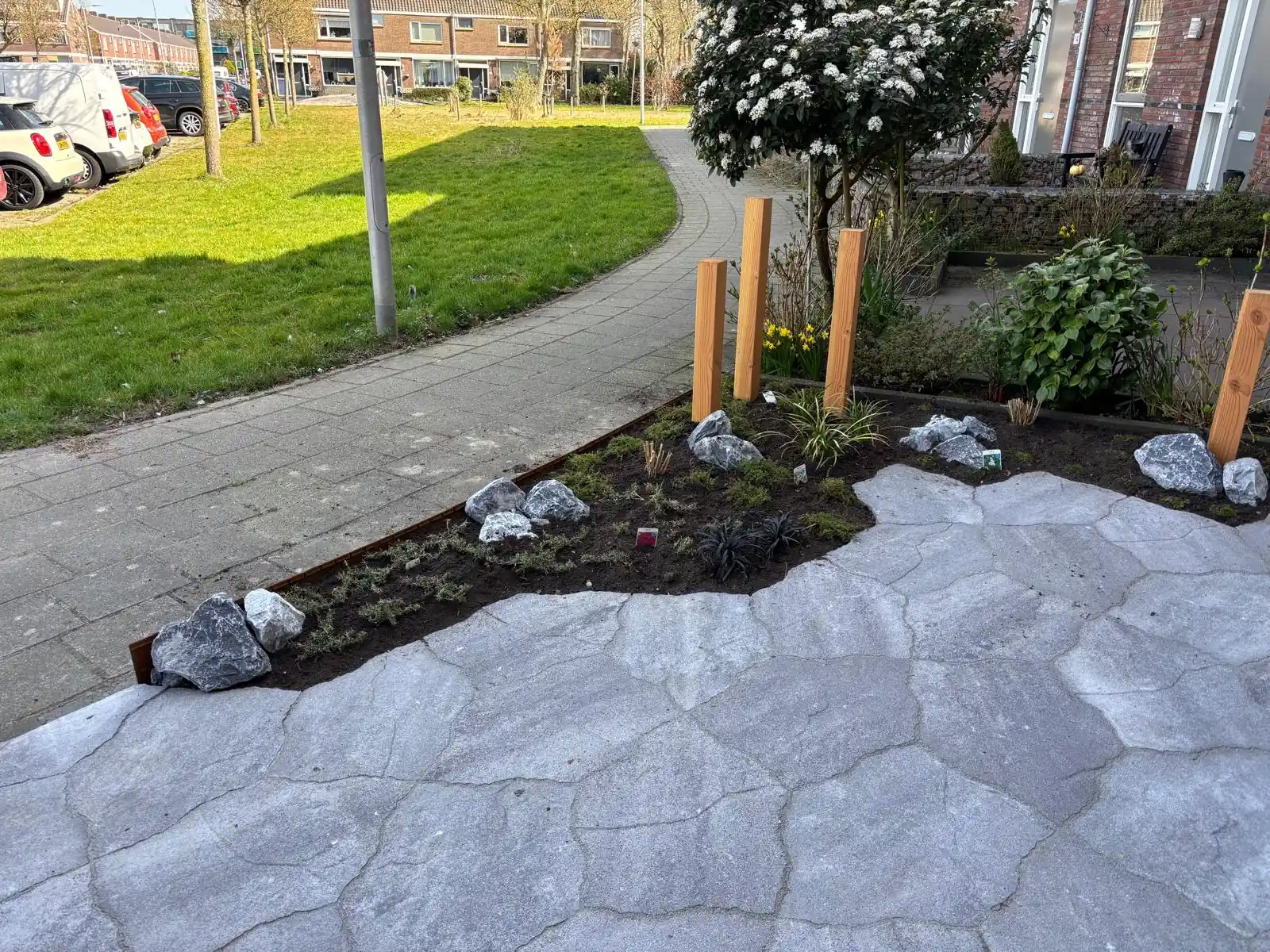 Border met keien en lage beplanting achter een cortenstalen kantopsluiting langs het trottoir, grenzend aan een terras van flagstones
